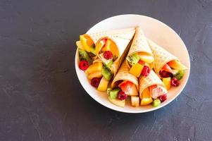 postre de frutas conos de gofre llenos de fruta en un plato blanco. el final del verano y el menú dulce. foto