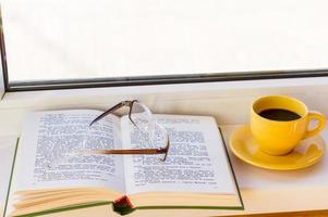 an open book with reading glasses and a cup of strong coffee on the windowsill. the concept of reading your favorite book. photo