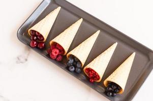 crispy waffle cones with summer berries on a plate of ceramics. healthy eating. photo