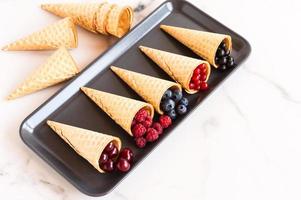 assortment of waffle cones with summer berries on a marble rectangular plate. great dessert. photo