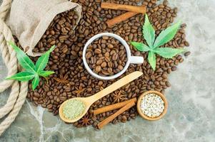 una composición de granos de café, una taza llena de granos de café aromáticos, semillas de cannabis y hojas de morijuana sobre un fondo de mármol. foto