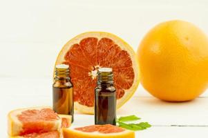 natural essential oil of grapefruit fruits in glass medical bottles with a dropper against the background of a white brick wall. photo