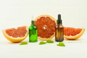 vitamin C serum, a bottle of organic grapefruit essential oil on a white background with grapefruit slices and lemon balm leaves photo