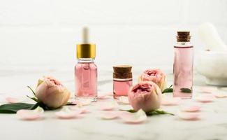 essential oil from rose petals, rose water in glass bottles with cork lid. buds and rose petals against the background of a white brick wall. photo