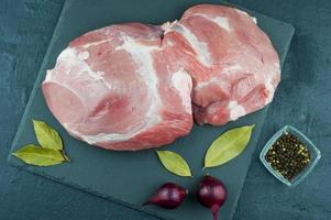 a large piece of fresh blue meat on a slate stone and a black background with laurel leaf, onion and pepper. top view. photo