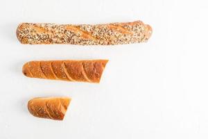 top view of a white background with a whole grain flour baguette with bran, seeds and two pieces of French baguette with sesame seeds. flat styling. photo