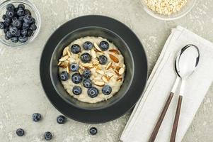 top view of a dark ceramic plate with oatmeal, ripe blueberries and almonds. delicious healthy breakfast. gray concrete background. photo