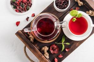 vista superior de una bandeja de madera con una tetera de vidrio y una taza blanca de té de hibisco. una bebida vitamínica útil rica en vitaminas. foto