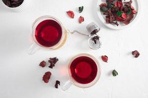 two glass transparent cups of hibiscus red tea on a white background with dried rose petals. top view. the concept of weight loss. photo