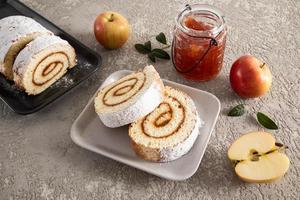 two ceramic trays with chopped pieces of apple biscuit roll with powdered sugar, a jar of apple jam, fresh fruit on a concrete background. photo