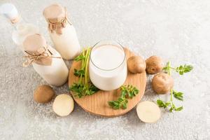 top view of a glass filled with potato milk, a bottle of plant milk and potato tubers. gray concrete background. photo