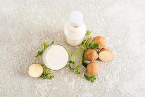 top view of a glass filled with potato milk, a bottle of plant milk and potato tubers. gray concrete background. photo