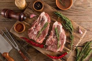 two steaks of raw farm pork on a wooden board with a sprig of drizzle, pepper, spices. top view, wooden rustic table. photo