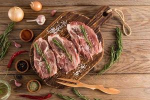 three steaks of farm pork on a wooden rustic cooking board with ingredients for cooking. top view. rustic table. photo