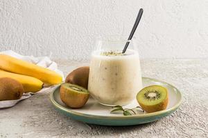 banana smoothie with pieces of kiwi and chia seeds in a glass against a background of gray concrete. a hearty energy breakfast or a snack. photo