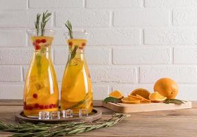 dos decantadores para agua con una bebida refrescante fría de naranja y bayas, con ramitas de romero y cubitos de hielo. agua Detox. foto