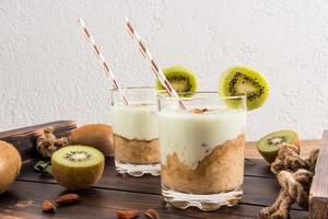 two glasses on a wooden tray with a banana-nut smoothie against a white textured wall and kiwi fruit. healthy organic breakfast. photo