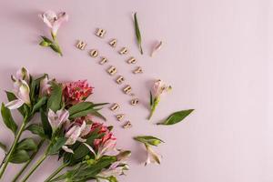 una composición festiva para el día de la madre a partir de hermosas flores primaverales e inscripciones en letras de madera. fondo rosa vista superior. foto