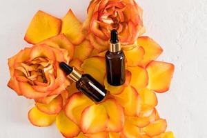 Top view of two bottles with a pipette lie on the petals of a tea rose . concept of natural organic essential oil or serum for face and body care. photo