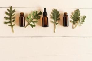 essential aromatic oil with natural ingredients against the background of a white wooden table with gray leaves of plants. flat lay. photo