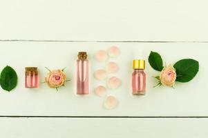 top view of the white wooden background with cosmetic bottles with rose oil and rose water for facial care. flat lay. photo