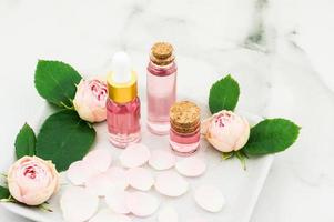 bottles of essential, cosmetic rose oil on a ceramic tray with rose petals and buds. the concept of skin care, beauty, well-being. photo