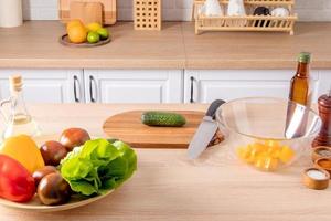 spread out on part of a modern kitchen with various items for cooking. a large dish with vegetables, a cutting board with a knife and a salad bowl. photo