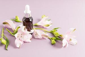 moisturizing liquid oil for the face, a cosmetic natural product in a bottle with a pipette made of glass a background of flowers alstroemerieae. photo