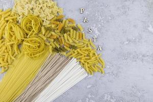 top view of various types of dry pasta and noodles on a grey background. letters - paste. photo