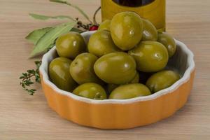 aceitunas verdes en un recipiente sobre fondo de madera foto