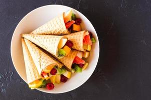 conos de gofre rellenos de fruta fresca picada en un plato blanco. vista superior. foto