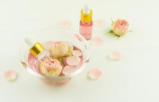 cosmetic rose oil in bottles with a pipette in a glass bowl on a white wooden table. the concept of natural self-care. photo