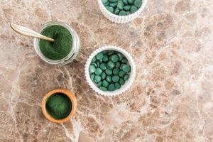 Top view of various containers with green powder and spirulina tablets to improve metabolism and strengthen the body. marble background. photo