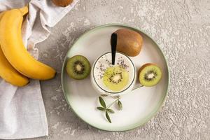 vista superior de un vaso de batido hecho de kiwi y plátano con semillas de chía. delicioso postre saludable. fuente de fibra dietética. fondo de hormigón gris. foto