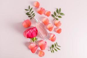 top view of the perfume product in glass flakrn against the background of rose petals and flower. pink pastel background. flat styling. photo