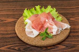 Prosciutto on wooden board and wooden background photo