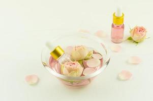 recipiente de vidrio con agua de rosas, flores y pétalos de rosas, botellas cosméticas con aceite de flor de zfir. aromaterapia, antiestrés. foto