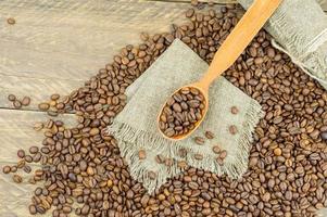 top view of a wooden spoon filled with coffee beans on a burlap napkin and a wooden coffee table. photo