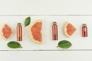 top view of bottles with a lid with grapefruit essential oil or cosmetic essence and fruit and green leaf slates. flat lay . white background. photo