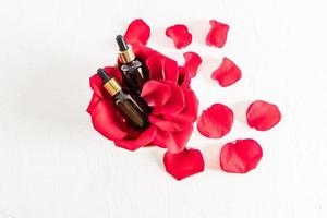 two glass bottles with a pipette with serum or cosmetic oil from rose petals for face and body care. top view. beautiful red rose petals. photo