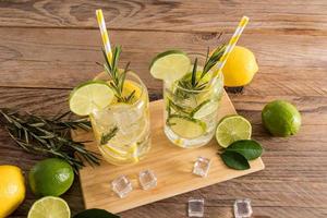 bebidas frías de verano con rodajas de cítricos y agua con gas en dos vasos sobre una mesa de madera. estilo rústico