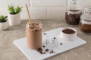 wonderful coffee with vanilla and cinnamon in a modern glass in the form of a jar of ice cubes on a white marble board. gray concrete background. photo