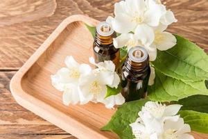 natural jasmine essential oil in two glass medical bottles with a dropper on a wooden tray among the flowers of jasmine. the concept of a spa. photo