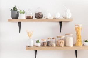 vista frontal de los estantes de la cocina con varios tarros ecológicos para almacenar productos a granel. vista frontal. pared blanca. cactus en macetas. foto