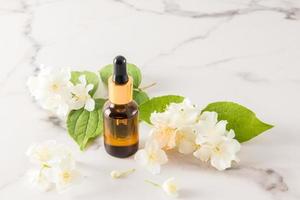whey based on jasmine oil in a cosmetic bottle of brown glass on a marble white background and fresh flowers of garden jasmine. photo