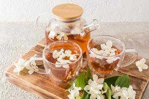 healing tavya tea with jasmine flowers in a glass kettle and cups on a wooden wallpaper board and cement background. the most popular tea. photo