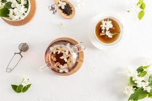 tea composition on a white background. glass teapot with jasmine tea, white forfor cup of tea, strainer, dry tea leaves. top view. photo