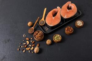 top view of the black background with two steaks of fresh raw salmon and mini bowls with nuts, flax and pumpkin seeds. healthy food . photo