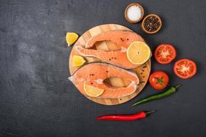 top view of two fresh salmon steaks on a round wooden board with lemon, pepper and tomatoes. the concept of healthy eating, cooking healthy food. photo