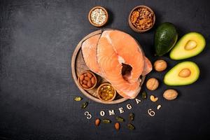 two raw salmon steaks on a round wooden tray surrounded by ripe avocado, nuts, seeds, omega3 capsules. top view. copy of the space. photo